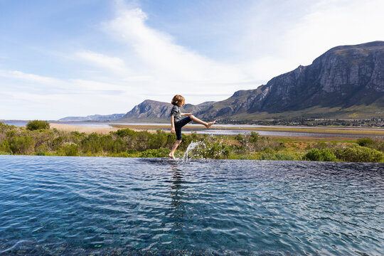 Eight year old boy walking around the edge of an infinity pool, mountain backdrop