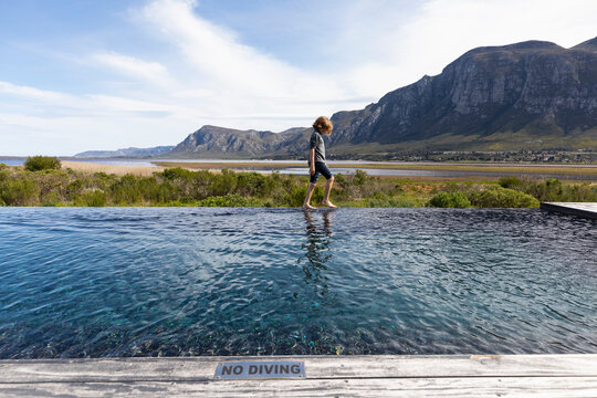 Eight year old boy walking around the edge of an infinity pool, mountain backdrop