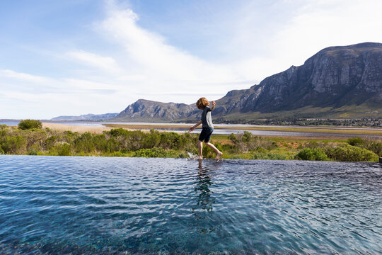 Eight year old boy walking around the edge of an infinity pool, a mountain backdrop