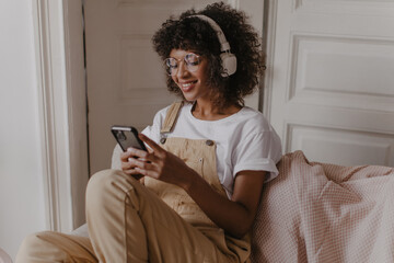 close-up of charming woman sitting on sofa in cozy room with phone in her hands. curly-haired...