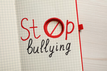 Open notebook with phrase Stop Bullying on white wooden table, top view