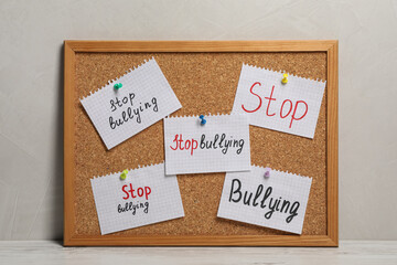 Notes with phrase Stop Bullying pinned to cork board on table near grey wall