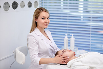 Young Woman enjoying anti aging facial massage. Woman is getting professional skin care at wellness center by nice smiling beautician. Relaxation, beauty, spa and face treatment, copy space