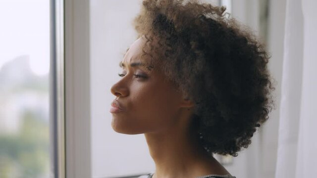 Beautiful young woman with afro hair thinking of problem, looking out the window