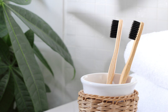 Two Bamboo Toothbrushes With Charcoal Bristles In The White Bathroom With Green Plant.