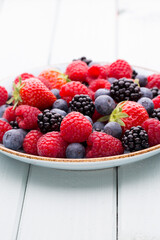 Fresh berry salad on blue dishes. Vintage wooden background.