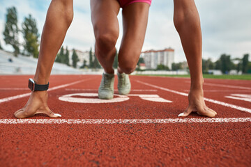 Close up shot of strong arms and legs of professional young female runner ready to race on track field at stadium