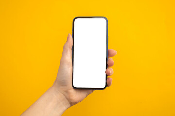 Person holding mobile phone with blank white screen on a yellow background, copy space photo