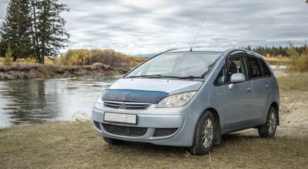 Obraz premium Car is parked on the bank of a river next to a yellow green autumn forest. Concept of beautiful nature and autumn mood