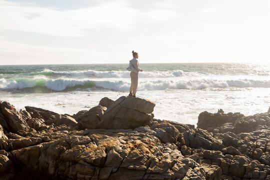 Teenage girl standing looking out to sea, surf rolling into the shore.