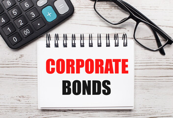 On a light wooden table calculator, glasses and a blank notepad with the text CORPORATE BONDS. Business concept