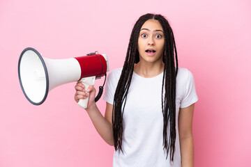 Teenager girl with braids over isolated pink background holding a megaphone and with surprise expression