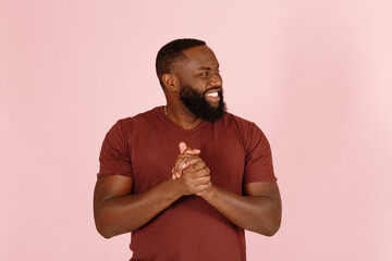 Smiling Afro-American man trickster rubs hands ready for cozy deal standing on light pink background in studio close view - 458951616