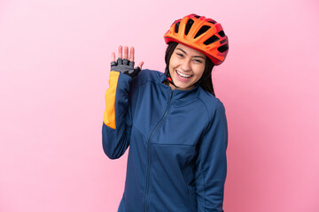 Teenager cyclist girl isolated on pink background saluting with hand with happy expression