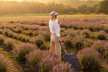 Beautiful young woman in lavender field standing with suitcase