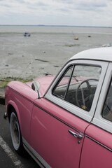 side of a vintage pink car parked in front of a beach