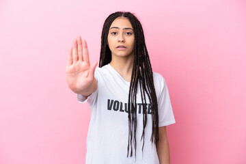 Teenager volunteer girl with braids isolated on pink background making stop gesture