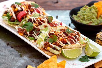 row of Tasty spicy and healthy Mexican street tacos served with various vegetables and salsa with chicken meat, beans   on slate with carne asada and al pastor in corn tortilla