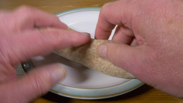 Closeup POV Shot Of A Mans Hands Rolling On A Plate A Soft, Tortilla Wrap, Made From Wholemeal Wheat And Filled With Salad, Then Adding Some Baked Potato Crisps / Chips.