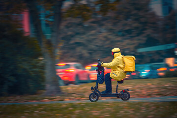 Delivery man in yellow raincoat riding electric scooter in rainy wether. Man delivering food in...