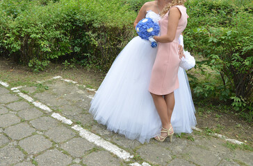 portrait of bride together with the bridesmaid in the park. the bride is holding a blue flower...