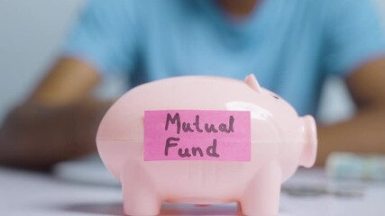 Concept of mutual fund investment, showing with hands placing coins inside the piggy bank with mutual fund sticker.