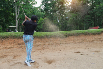 Golfer hitting golf ball on bunker of sand in course.