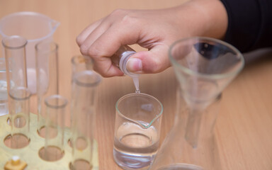 Close-up of a student's hand dripping a chemical solution into a glass. A schoolboy performs a task at the workplace. The concept of children's education, teaching knowledge, skills and abilities.