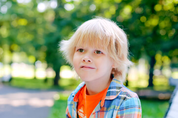 Cute blonde caucasian kid sitting on the bench at the park. Summer vacation happy childhood