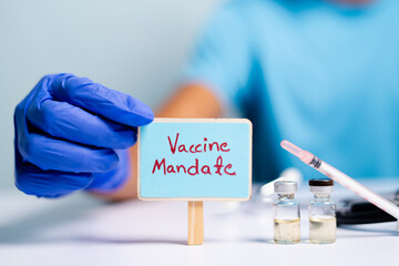 Concept of coronavirus or covid-19 vaccine mandate, showing with doctor hands with gloves by placing sign board next to vaccine shots and syringe - obrazy, fototapety, plakaty