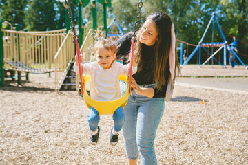 Happy mother with two year sit on the swing