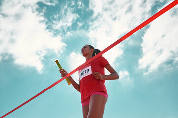 Low angle view of female young athlete with baton reaching the finish line at track field during...