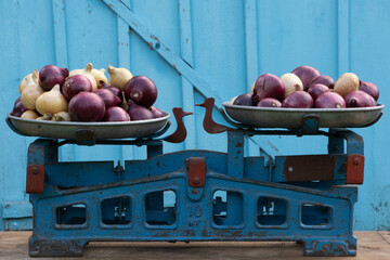 Strong red and white onions on two bowls of old Soviet-era scales against a dilapidated light blue...