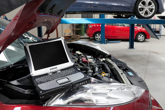 Car in a workshop and a computer running diagnostics on the engine.