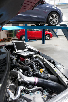 Car in a workshop and a computer running diagnostics on the engine.