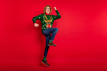 Photo of funny lucky young guy dressed print pullover smiling jumping rising arms empty space isolated red color background