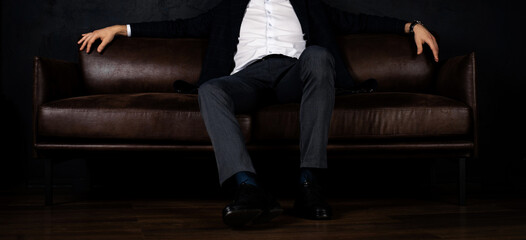 Unrecognizable stylish macho man sits relaxed on the sofa in the dark.