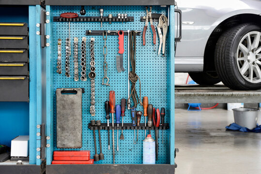 Tools on a blue board in a storage cabinet,organised in rows,at an auto repair shop.