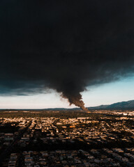 Aerial view of dense buildings and a column of black smoke rising up and covering the sky