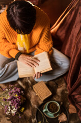 Fototapeta na wymiar Beautiful woman in orange sweater reading a book and enjoying her coffee
