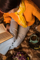 Beautiful woman in orange sweater reading a book and enjoying her coffee