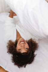 medium shot image of lawless smiley woman who is laying in bed with white linens. female looks...