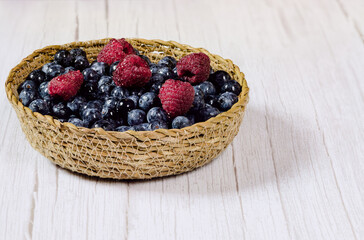 Fresh blueberries and raspberries with drops of water in a small wicker basket. Fresh fruit washed with water and ready to eat. Vegan food. Healthy food concept.