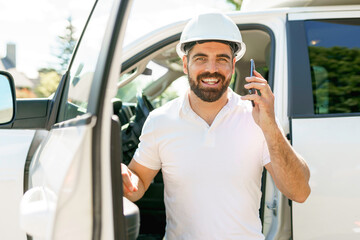 Man engineer builder wearing a white hard hat, shirt in front of his pickup using cellphone - obrazy, fototapety, plakaty