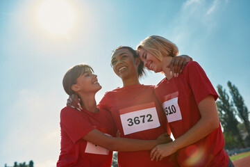 Portrait of cheerful diverse young female athletes wearing t shirts with number standing together, ready for the marathon