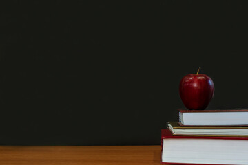 red apple on stack of books on wooden table and chalkboard page background