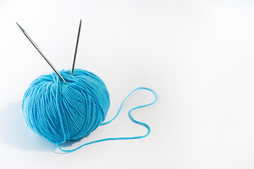 A ball of blue yarn with knitting needles on a white background. Women's needlework
