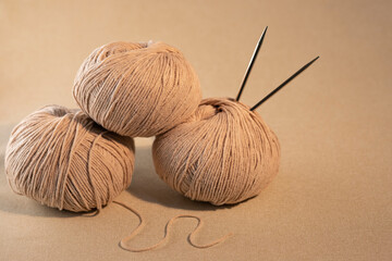 Balls of beige yarn with knitting needles. Women's needlework