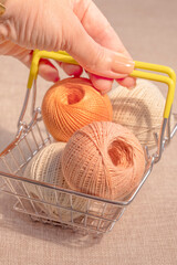 A woman's hand holds a metal basket with balls of knitting thread