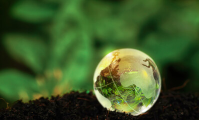 Crystal Earth On Soil In Forest With Sunlight - The Environment - Earth Day Concept. glass globe on...